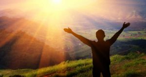 Beautiful photo of man lifting his arms and the sun shining above mountains